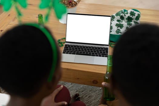 African american couple on st patrick's day video call using laptop with copy space on screen. staying at home in isolation during quarantine lockdown.