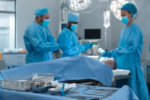 Diverse male and female doctors wearing face masks and surgical overalls in operating theatre. medicine, health and healthcare services during coronavirus covid 19 pandemic.
