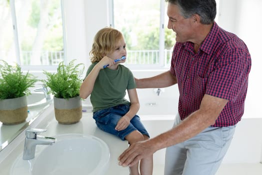 Smiling caucasian grandfather in bathroom with grandson brushing teeth sitting beside basin. staying at home in isolation during quarantine lockdown.