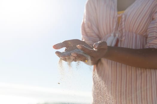 Mixed race woman on beach holiday spilling sand. outdoor leisure vacation time by the sea.