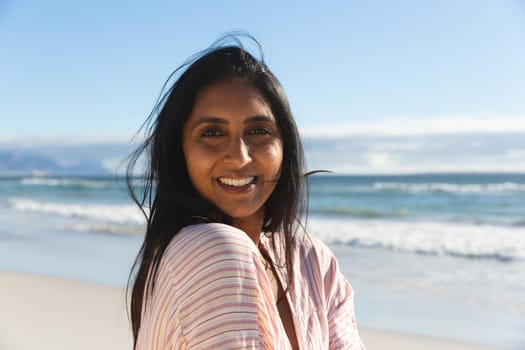 Portrait of smiling mixed race woman on beach holiday looking to camera. outdoor leisure vacation time by the sea.