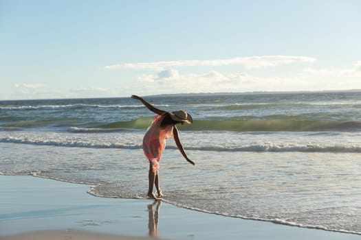 Mixed race woman wearing straw hat walking along the seashore with spread hands. vacation outdoor leisure time by the sea.