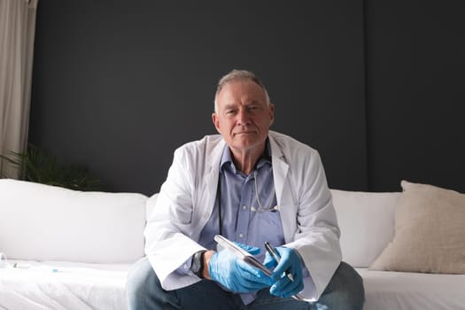 Caucasian senior male doctor holding notebook listening during consultation video call. telemedicine online during quarantine lockdown.