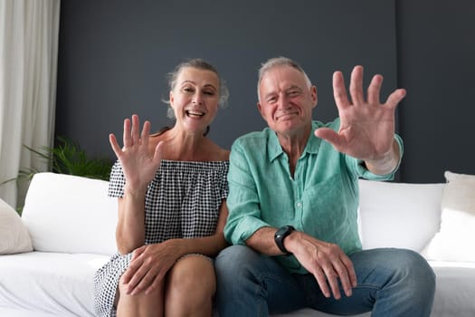 Happy caucasian senior couple in living room, on couch making video call, waving and smiling. staying at home in isolation during quarantine lockdown.