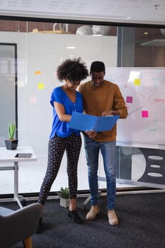 Diverse male and female colleagues standing having discussion with whiteboard in background. independent creative design business.