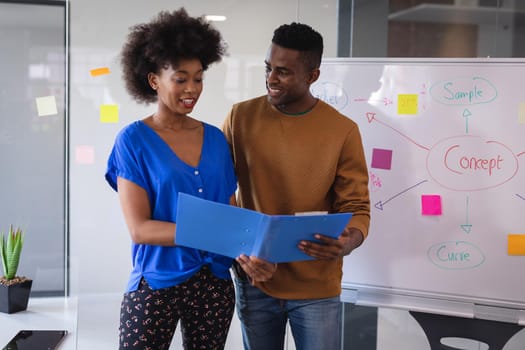 Diverse male and female colleagues standing having discussion with whiteboard in background. independent creative design business.