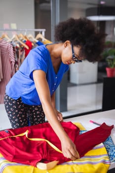 Mixed race fashion designer working in office with fabrics on the table and clothes in background. independent creative design business.