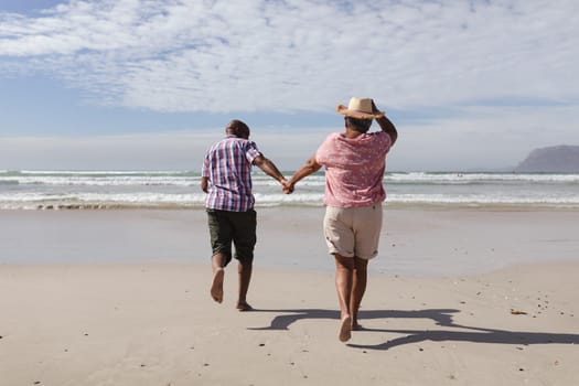 Rear view of senior african american couple holding hands running on the beach. travel vacation retirement lifestyle concept