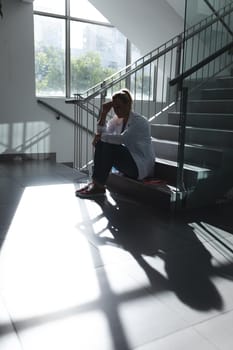 Caucasian female doctor sitting on sunny hospital staircase and worrying. medicine, health and healthcare services.