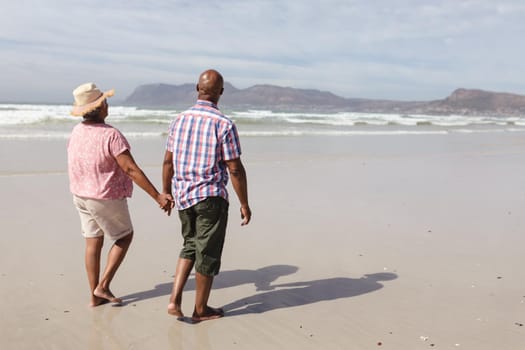 Senior african american couple holding hands walking on the beach. travel vacation retirement lifestyle concept
