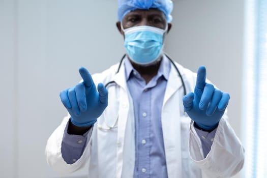 African american male doctor wearing face mask using virtual interactive interface. medicine, health and healthcare services during coronavirus covid 19 pandemic.