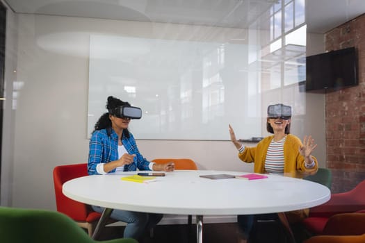 Diverse female colleagues sitting at work wearing virtual reality set and playing. independent creative design business.