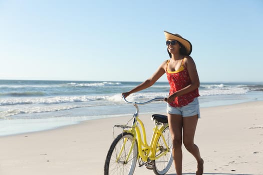 Happy mixed race woman on beach holiday walking with bicycle. outdoor leisure vacation time by the sea.