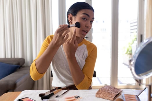 Mixed race gender fluid man making makeup vlog putting on foundation powder with brush and talking. staying at home in isolation during quarantine lockdown.