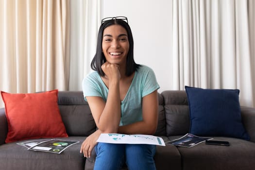 Mixed race gender fluid man working at home making video call with documents, smiling. staying at home in isolation during quarantine lockdown.