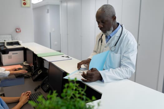 African american doctor standing in hospital corridor smiling to camera. medicine, health and healthcare services.
