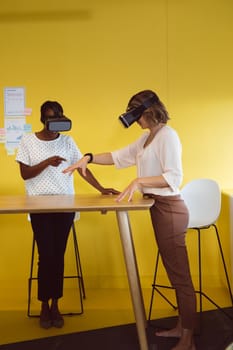 Diverse businesswomen standing at desk using vr headset at work. independent creative business at a modern office.