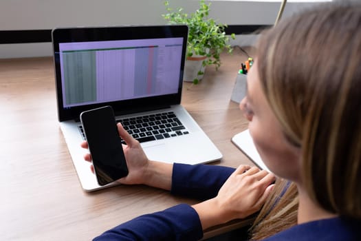 Caucasian businesswoman sitting at desk having video call conversation using smartphone. business in a modern office.