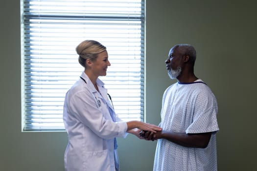 Diverse female doctor and male patient in hospital room smiling to each other. medicine, health and healthcare services.