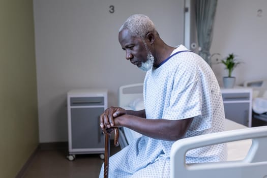 African american male patient sitting on hospital bed holding cane. medicine, health and healthcare services.