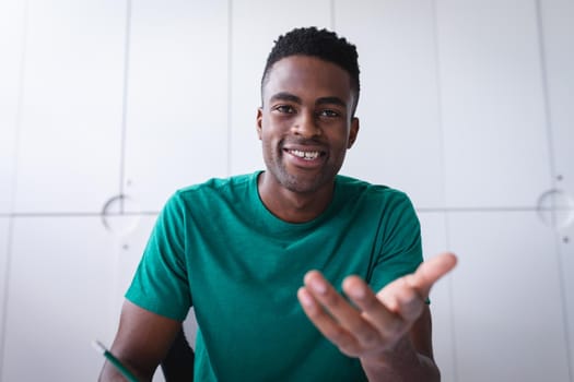 African american businessman sitting in office having video call and making notes. independent creative design business.