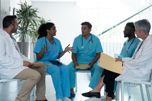 Diverse male and female doctors sitting in hospital corridor and discussing. medicine, health and healthcare services.