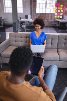 Diverse male and female colleagues working sititng on sofa in office using computer and tablet. independent creative design business.