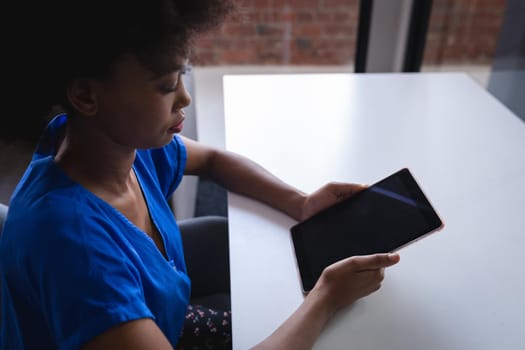 Mixed race businesswoman sitting in office using tablet with blank screen. independent creative design business.