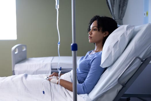 Mixed race female patient sitting in hospital bed wearing fingertip pulse oximeter and iv drip. medicine, health and healthcare services.