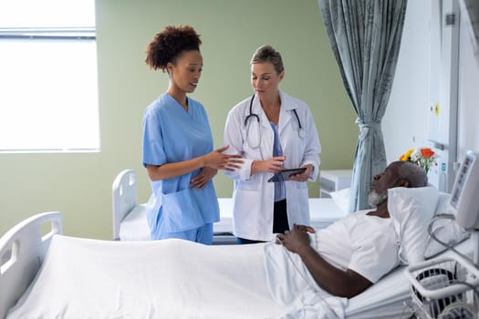 Two diverse female doctors and african american male patient in hospital room talking. medicine, health and healthcare services.