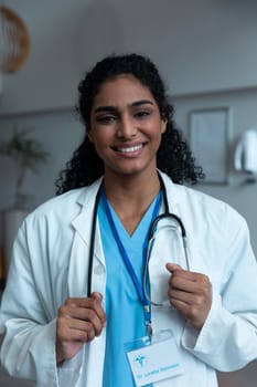 Portrait of smiling mixed race female doctor with stethoscope wearing lab coat in hospital. medicine, health and healthcare services during covid 19 coronavirus pandemic.
