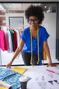 Happy mixed race fashion designer working in office with tailor centimeter on neck. independent creative design business.