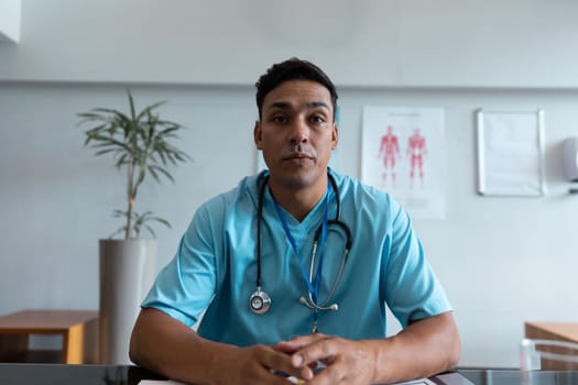 Mixed race male doctor at desk talking and gesturing during video call consultation. telemedicine, online healthcare services during quarantine lockdown