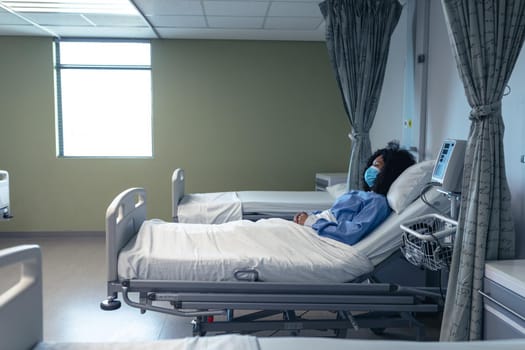 African american female patient lying in hospital bed wearing face mask. medicine and health services during coronavirus covid 19 pandemic.
