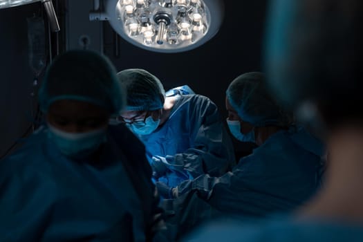 Diverse group of male and female surgeons in operating theatre wearing face masks performing surgery. medicine, health and healthcare services during coronavirus covid 19 pandemic.