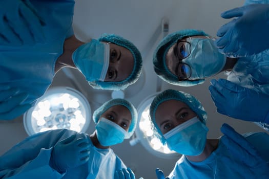 Diverse group of male and female surgeons in operating theatre wearing face masks performing surgery. medicine, health and healthcare services during coronavirus covid 19 pandemic.