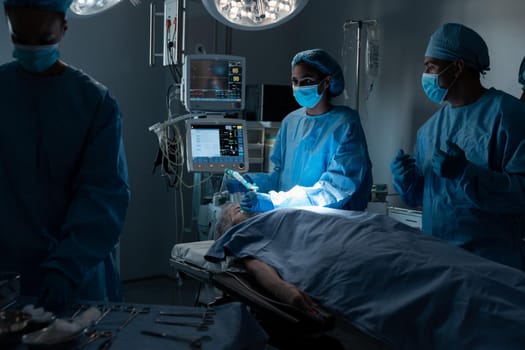 Diverse surgeons with face masks and protective clothing during operation, sedating patient. operating theatre. medicine, health and healthcare services during covid 19 coronavirus pandemic.