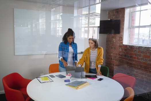 Diverse female colleagues standing at meeting room discussing looking at laptop. independent creative design business.