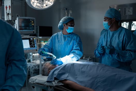 Diverse surgeons with face masks and protective clothing during operation, sedating patient. operating theatre. medicine, health and healthcare services during covid 19 coronavirus pandemic.