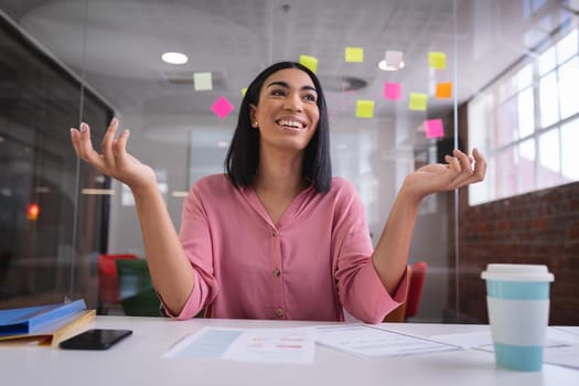 Happy mixed race businesswoman sitting at desk while having a video call smiling. independent creative design business.