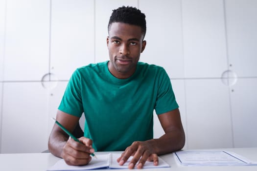 Happy african americen businessman sitting at desk while having a video call making notes. independent creative design business.