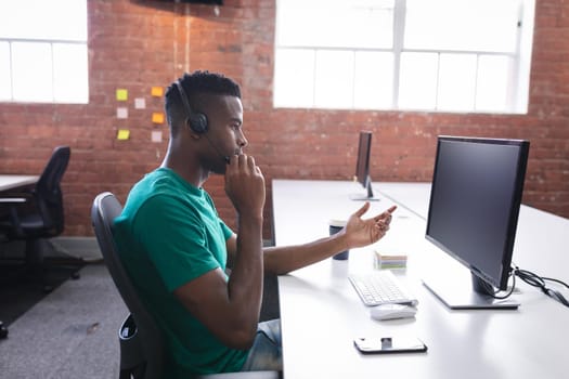 African american businessman having video call sitting in front of computer using headphones. independent creative design business.