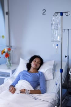 Mixed race female patient lying asleep in hospital bed wearing fingertip pulse oximeter and iv drip. medicine, health and healthcare services.