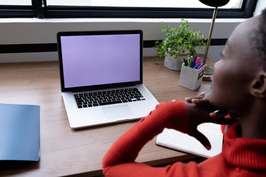 African american businesswoman sitting at desk having video call using laptop with copy space. business in a modern office.