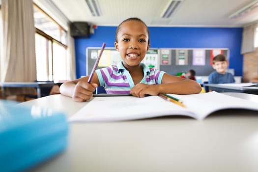 Portrait of african american girl smiling while sitting on her desk at elementary school. school and education concept