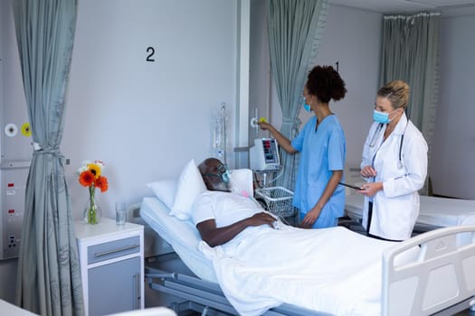 Mixed race female doctor wearing face mask changing oxygen level of male patient. medicine, health and healthcare services during coronavirus covid 19 pandemic.