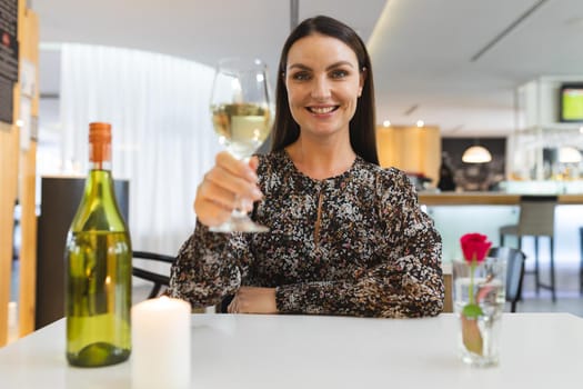 Caucasian woman sitting at table in restaurant on dinner date smiling holding wine glass. friends talking to each other sitting in a restaurant.