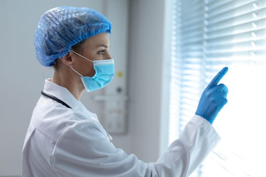 Caucasian female doctor wearing face mask using virtual interactive interface. medicine, health and healthcare services during coronavirus covid 19 pandemic.