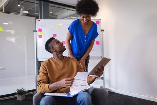 Diverse male and female colleagues having video call on tablet with whiteboard in background. independent creative design business.