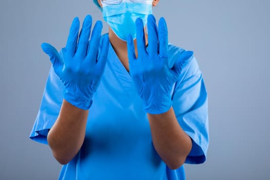 Mid section of female surgeon wearing surgical gloves against grey background. healthcare and medical professionalism concept